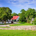 Maalaisidyllisessä maisemassa kiviaita ja rakennuksia kirkkaana kesäpäivänä.