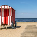 Punavalkoinen rantakärry hiekkarannalla puisen kävelylaiturin vieressä, taustalla meri.