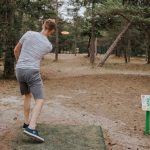 Poika heittää frisbeegolf kiekkoa radalla