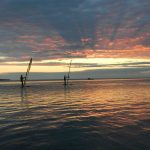 Kolme lainelautailijaa vesillä auringonlaskussa