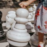 Pieni tyttö siirtää jättikokoista valkoista shakkinappulaa ulkopelilaudalla