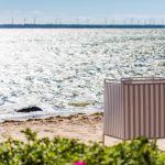 Laulasmaan rannalla seisoo puna-valkoraidallinen uimavaatteidenvaihtokoppi, niemenkärjessä siintää rivi tuulimyllyjä