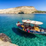 Turkoosin sininen ja kirkas merivesi, kalastajavene etualla ja uimaranta vastarannalla