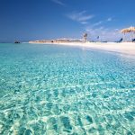 Vaalealla rantahiekalla aurinkotuoleja turkoosin sinisen veden äärellä