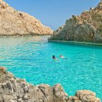 Mies ja nainen uimassa kirkkaan turkoosissa vedessä upeiden kallioiden keskellä