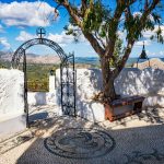 Maisema luostarin etupihalta valkoisen aidan ja metalliportin takaa.