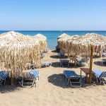 Falirakin rannalla sinivalkoisia aurinkotuoleja ja kaislakattoisia aurinkovarjoja.