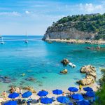 Panoraamanäkymä rannan yli kirkasvetiseen, kallioiden kehystämään poukamaan.