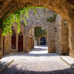 Keskiaikainen kuja, muuratun kaaren takaa roikkuu köynnöksiä.