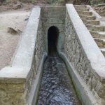 Vesi virtaa kapeaan tunneliin maan alle.