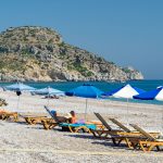 Ihmisiä aurinkopedeillä rannalla sinivalkoisten päivävarjojen alla.