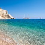 Purjelaiva ja moottorivene turkoosilla merellä kallion edustalla.