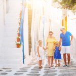 Nelihenkinen perhe kävelemässä kirkkaana päivänä kreikkalaisella kujalla.