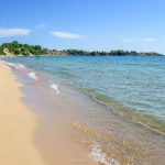 Ihmisiä ottamassa aurinkoa ja kävelemässä hiekkarannalla turkoosin meren äärellä.