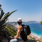 Mies katsoo alas rannalle vesipullolla varustettu reppu selässä.