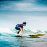 Nuori poika surffilaudalla pienessä aallossa.