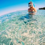 Nuori poika noussut kirkkaasta vedestä snorklaamasta uimalasit päässä.