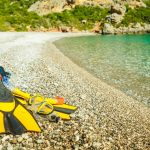 Keltaiset räpylät, uimalasit ja snorkkeli sileäkivisellä rannalla.