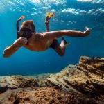 Mies ui veden alla räpylät jalassa ja pitää nenästä kiinni.