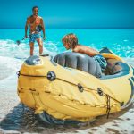 Isä kävelee hymyillen kohti kumiveneessä olevaa poikaa rannalla.