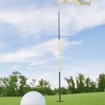 Lähikuvassa golfpallo viheriöllä, taustalla lipulla merkitty reikä.
