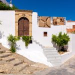 Valkoinen, kulmikas talo, jonka kattoterassin kaiteella roikkuu mattoja.