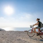 Nuori nainen punaisen pyörän selässä aurinkoisena päivänä mäen päällä.