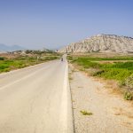 Kaksi ihmistä kauempana skootterin kyydissä hiljaisella maantiellä aukean keskellä.