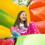 Tyttö istuu nauraen värikkäässä pomppulinnassa.
