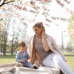 Nuori äiti katsoo pientä lastaan kirsikkapuun alla puistossa.