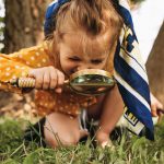 Polvillaan oleva pieni lapsi tutkii nurmikkoa suurennuslasilla.