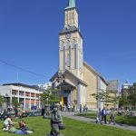 Ihmisiä nauttimassa kesäpäivästä puistossa Tromssan Tuomiokirkon edustalla.