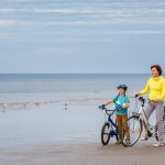 Äiti ja poika hymyilevät rannalla pyörien kanssa seisten.