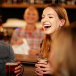 Mies ja nainen nauravat olutlasit käsissään baaritiskin edessä.