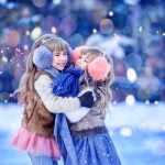 Kaksi pientä tyttöä juhlavissa vaatteissa isot korvalaput päässään halaavat nauraen.