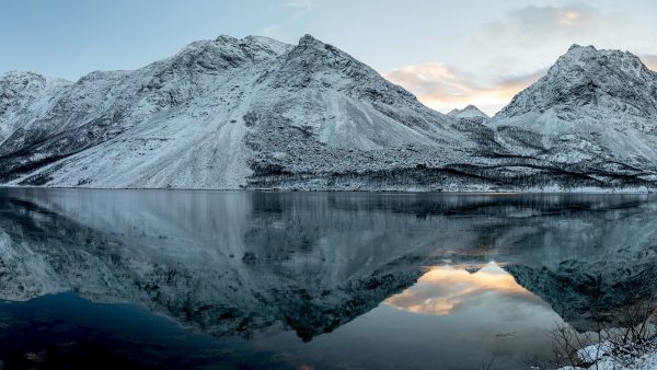 Tummansävyiset lumiset alpit veden äärellä