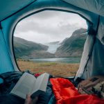 Näkymä teltasta kohti Svartiseniä. Henkilö makoilee kirja kädessä ja katsoo maisemaa.
