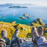 Kaksi henkilöä istuu meren yllä kalliolla vaelluskengät jalassa.