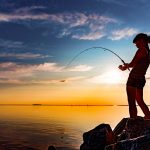 Nuori nainen kalastaa ilta-auringon paistaessa.