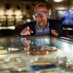 Silmälasipäinen mies katselee historiallisia esineitä museon vitriinissä.