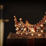 Lähikuva keskiaikaisesta kruunusta, taustalla miekka.