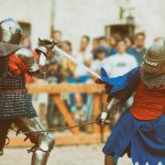 Keskiaikaisiin ritariasuihin pukeutuneet hahmot miekkataisteluesityksessä.