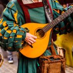 Keskiaikaiseksi trubaduuriksi pukeutunut henkilö esiintymässä.