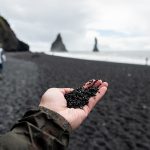 Henkilö pitää kädessään rannan mustaa hiekkaa.