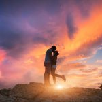 Pariskunta suutelee kalliolla auringonlaskussa