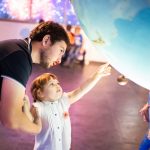 Pieni lapsi osoittaa tiedenäyttelyssä isälleen mielenkiintoista kohdetta.