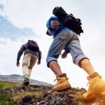 Kaksi vaeltajaa nousee mäkeä kallioisessa maastossa.