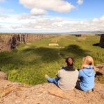 Kaksi retkeilijää istuu kallion reunalla ja katselee Asbyrgin kanjonia.