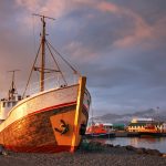 Kalastaja-alus maihin vedettynä venesatamassa auringonlaskun kajossa.