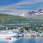 Akureyrin kaupunki mereltä kuvattuna, risteilyaluksia sekä pienempi laiva kaupungin edustalla.